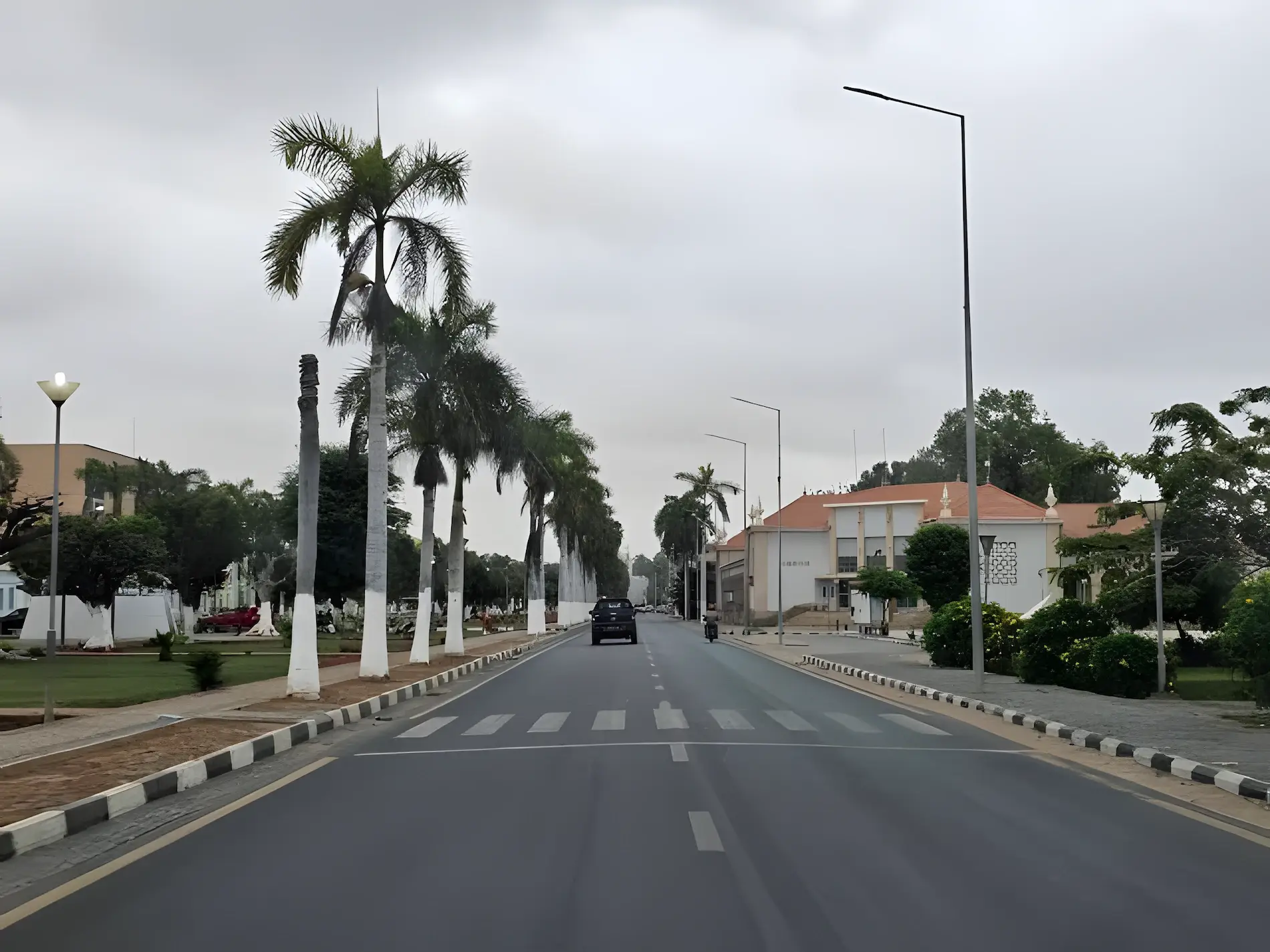 Avenue bordée de palmiers à Viana, à l’est de Luanda, avec un pick-up sur la route et des bâtiments bas au loin